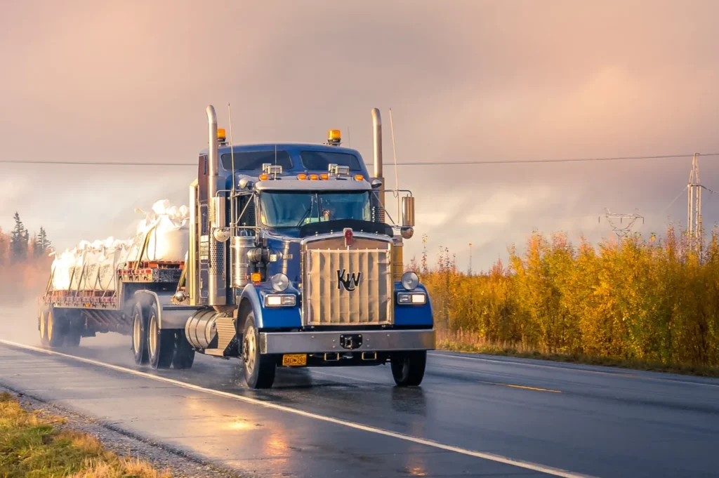 Large blue semi-truck hauling materials on a wet road during sunset, representing potential equipment failure risks in El Paso truck accidents.