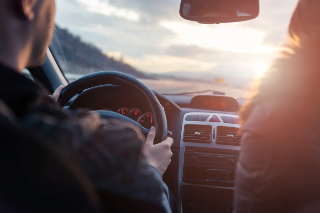 View from the backseat of a car showing a driver at the wheel and a passenger during a sunset drive, symbolizing a ride-share experience.