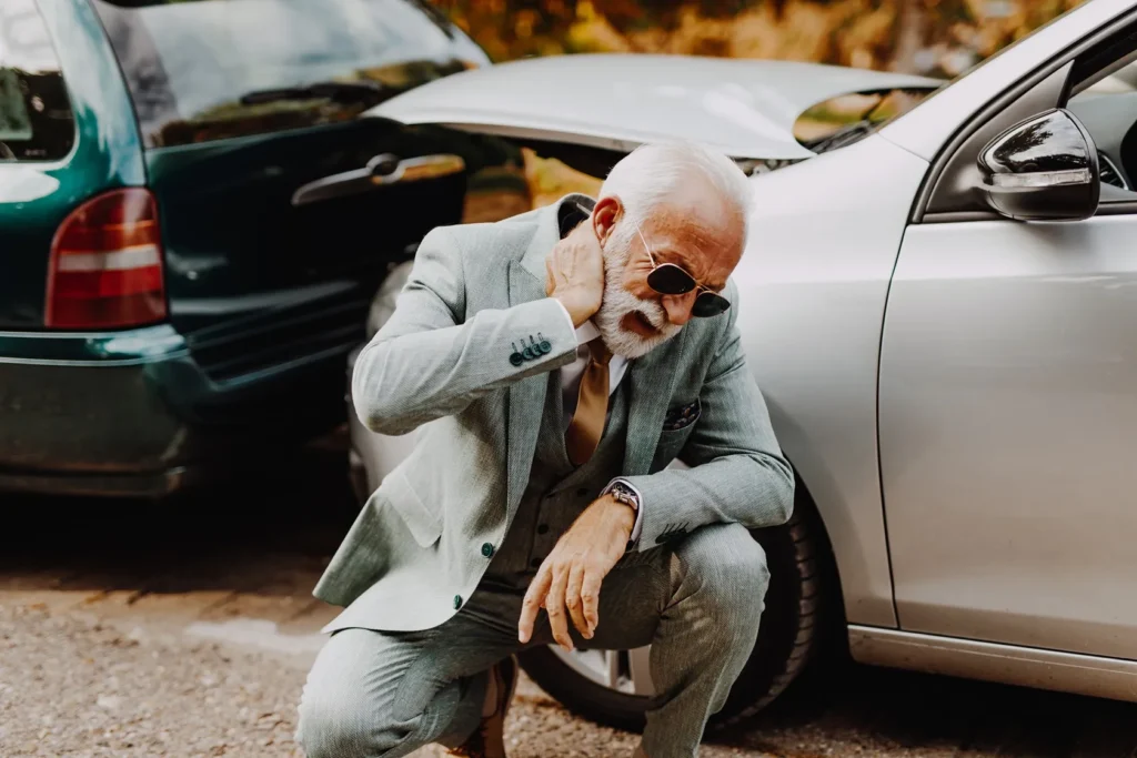 Older man in a suit holding his neck in pain after a rear-end car accident.