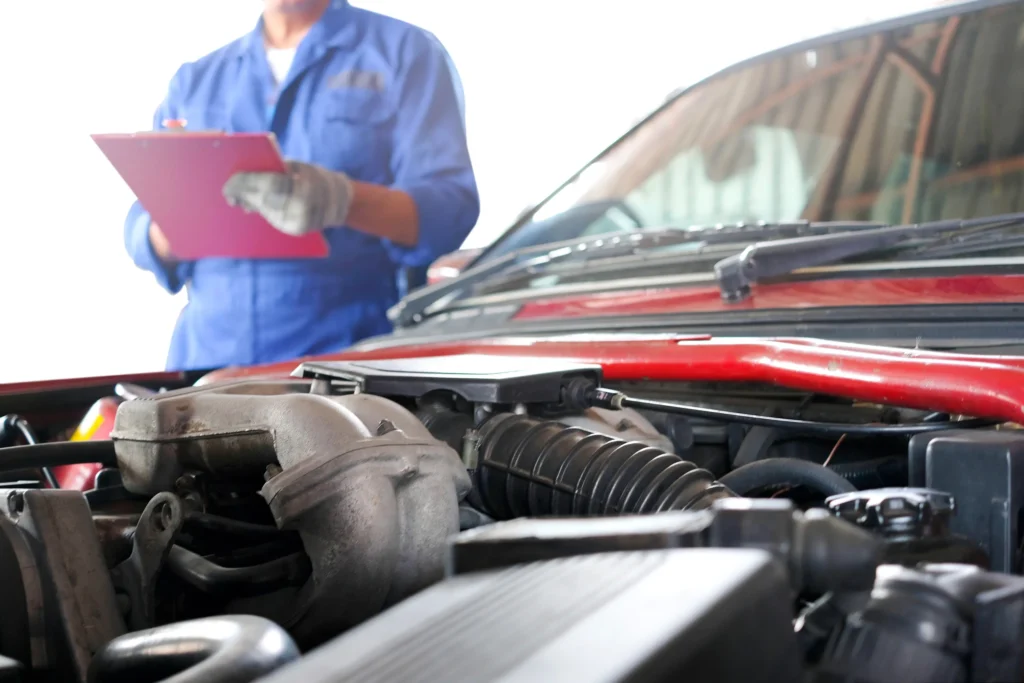 Mechanic in blue uniform holding a clipboard while inspecting a car engine in Texas.